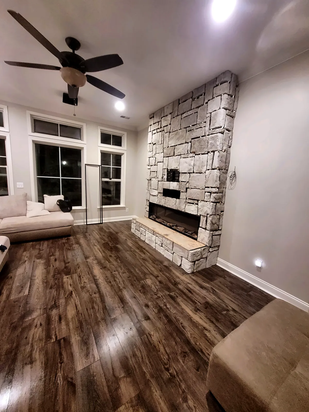 Stone fireplace wall in open living room with wood floors