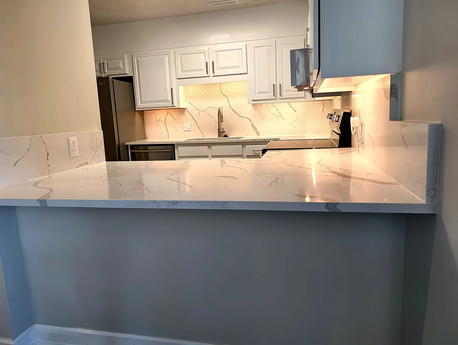 White kitchen with marble-look quartz peninsula and under-cabinet lighting