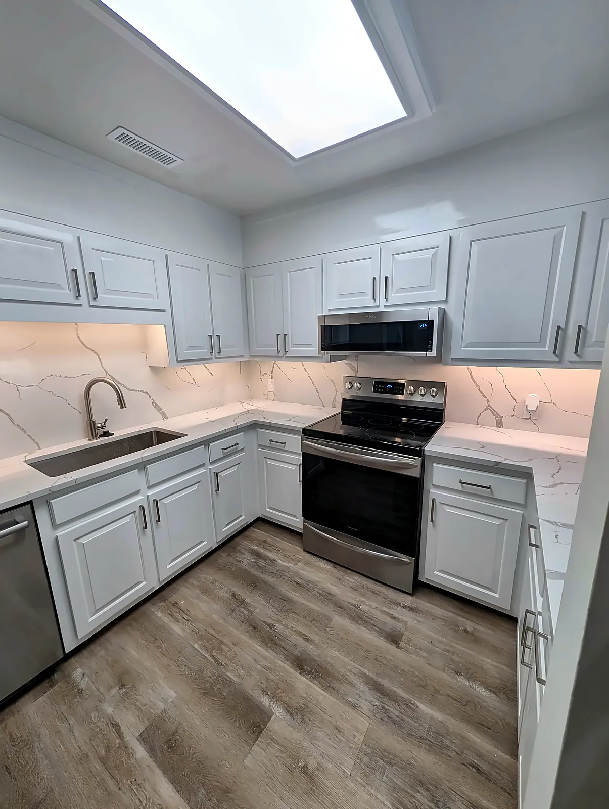 L-shaped white kitchen with skylight and stainless appliances