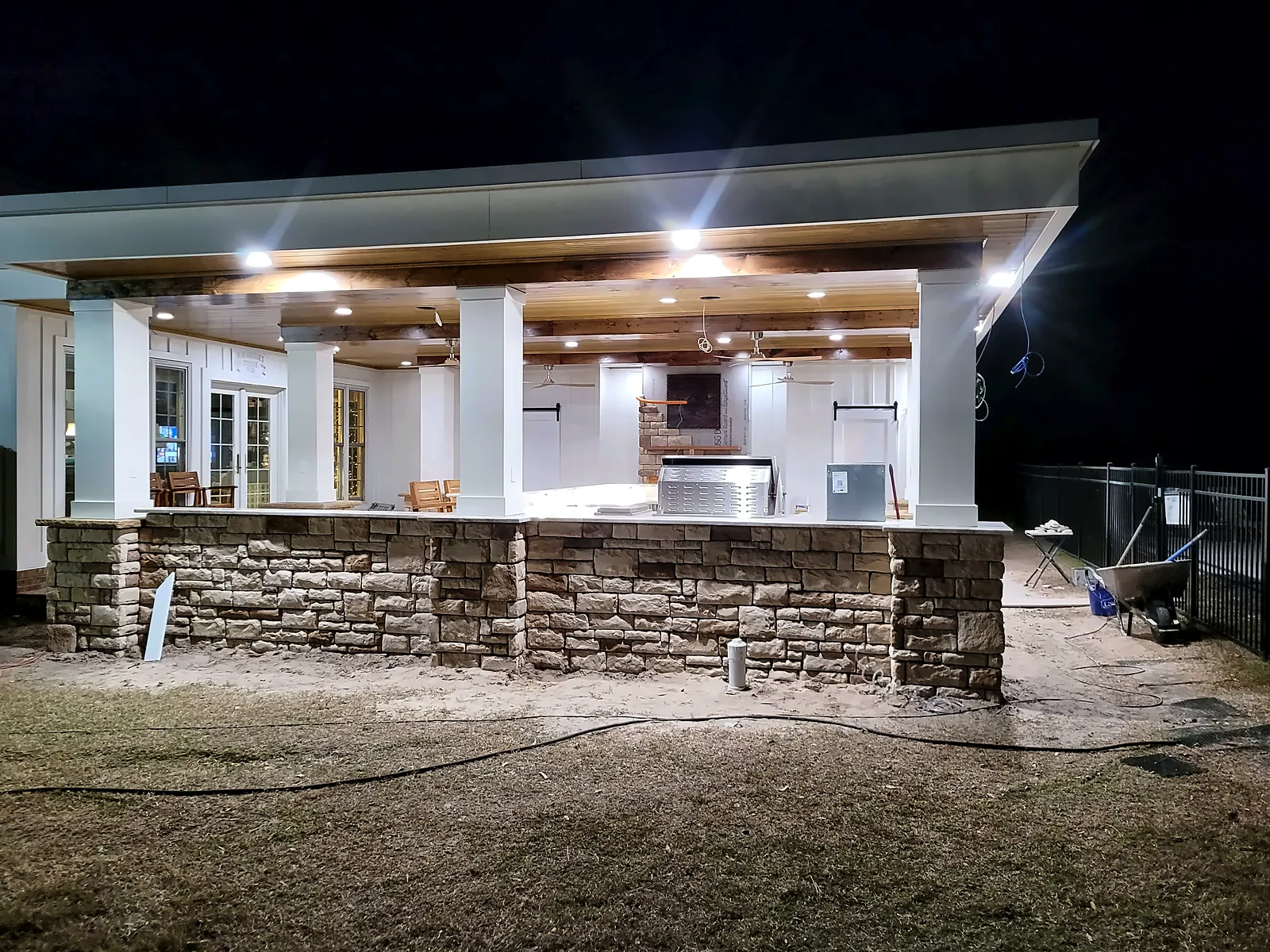 Covered outdoor living pavilion at dusk with stacked-stone base and white columns