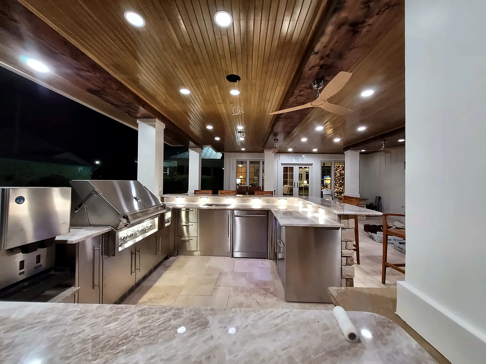 Outdoor kitchen and bar under a stained wood ceiling at night