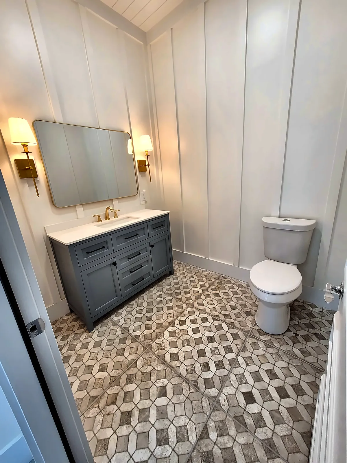 Pool house bathroom with patterned tile floor, grey vanity and sconces