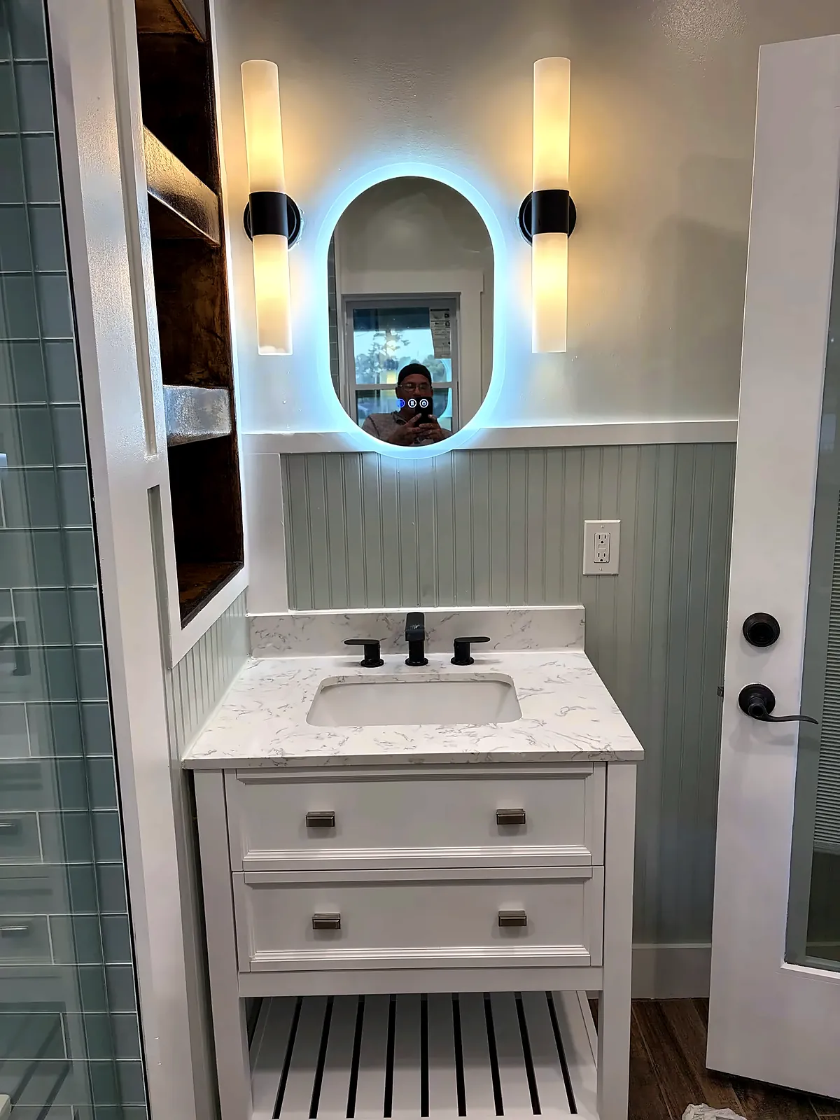 White vanity with backlit oval mirror and black sconces