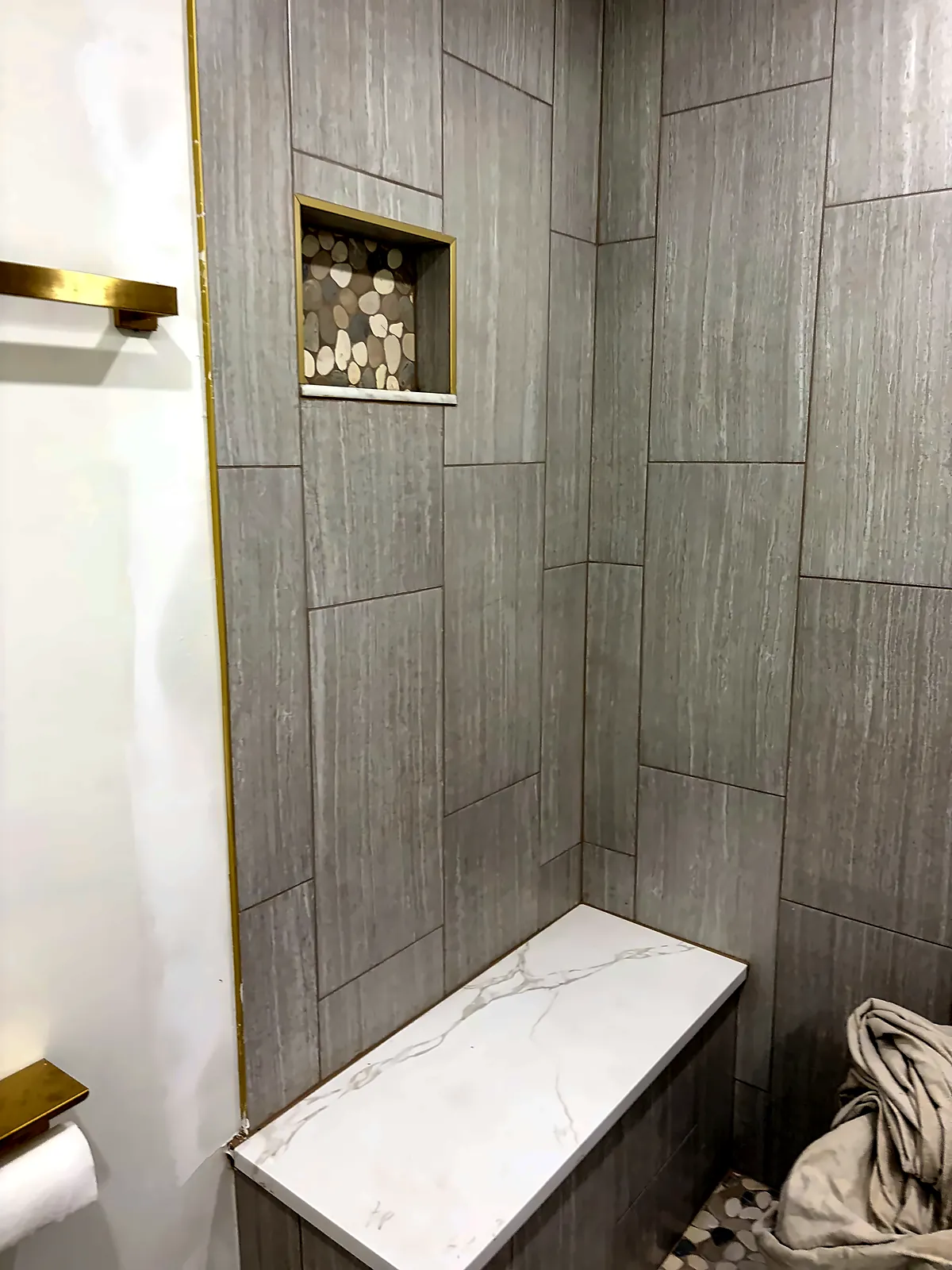 Stacked grey tile shower with gold fixtures and bench